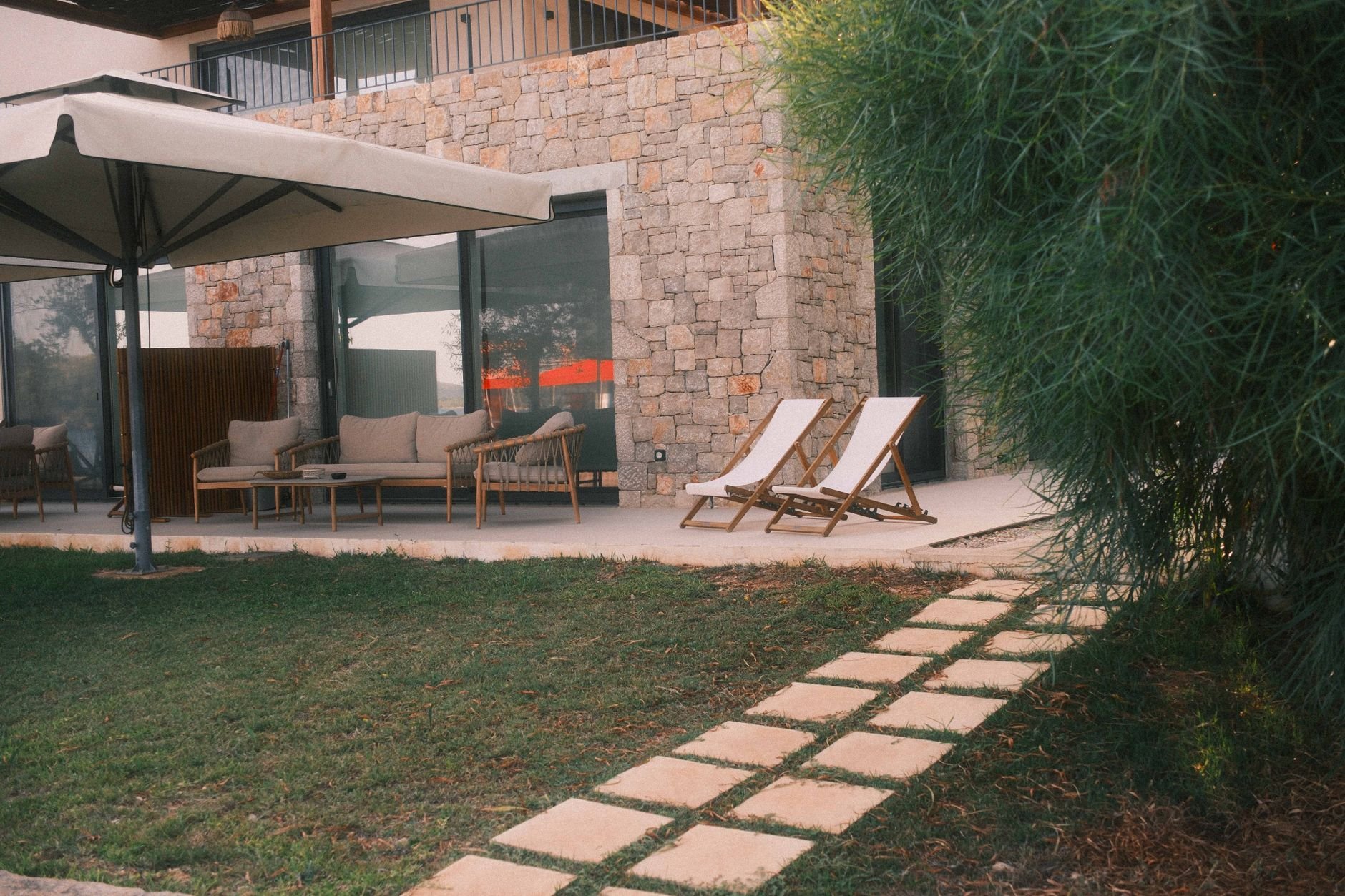 Relax in style on a beautiful stone patio with outdoor furniture, greenery, and loungers